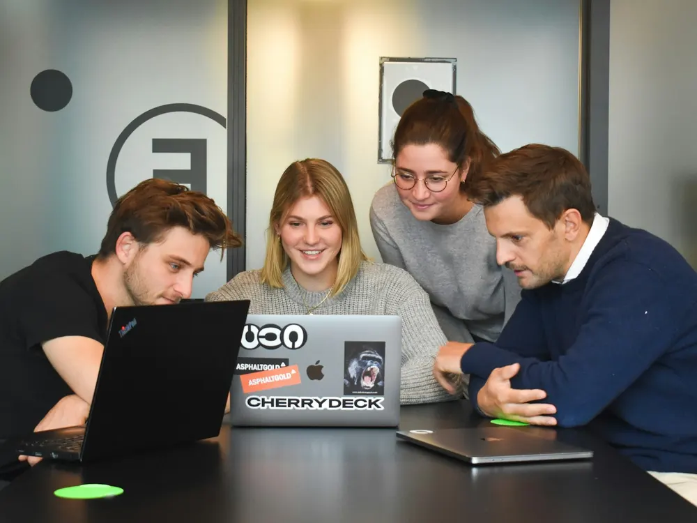 A smiling team working together around laptops in a bright office